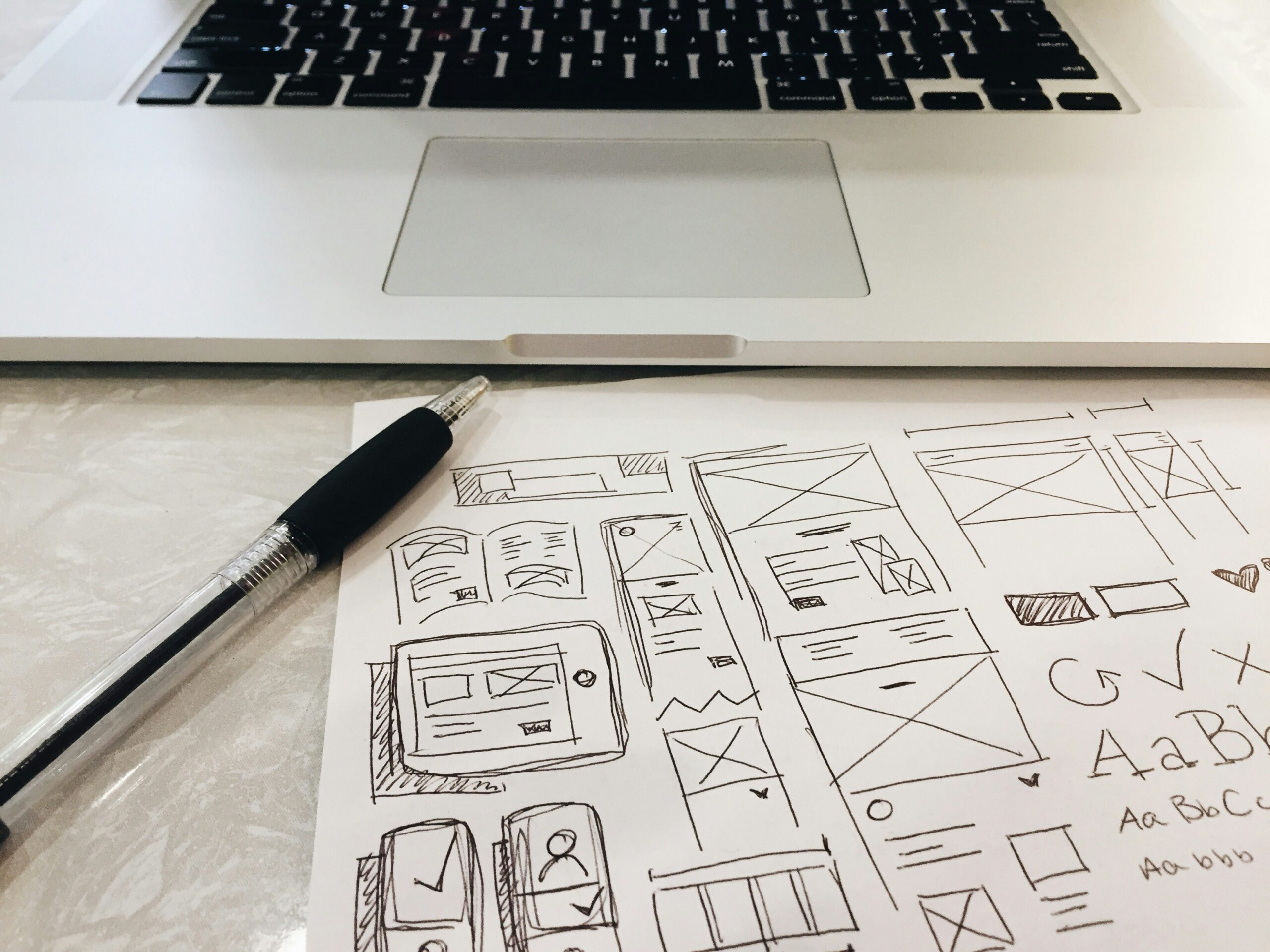 Hand-sketched website wireframes on paper beside a laptop