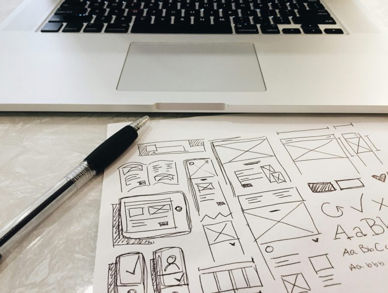Hand-sketched website wireframes on paper beside a laptop